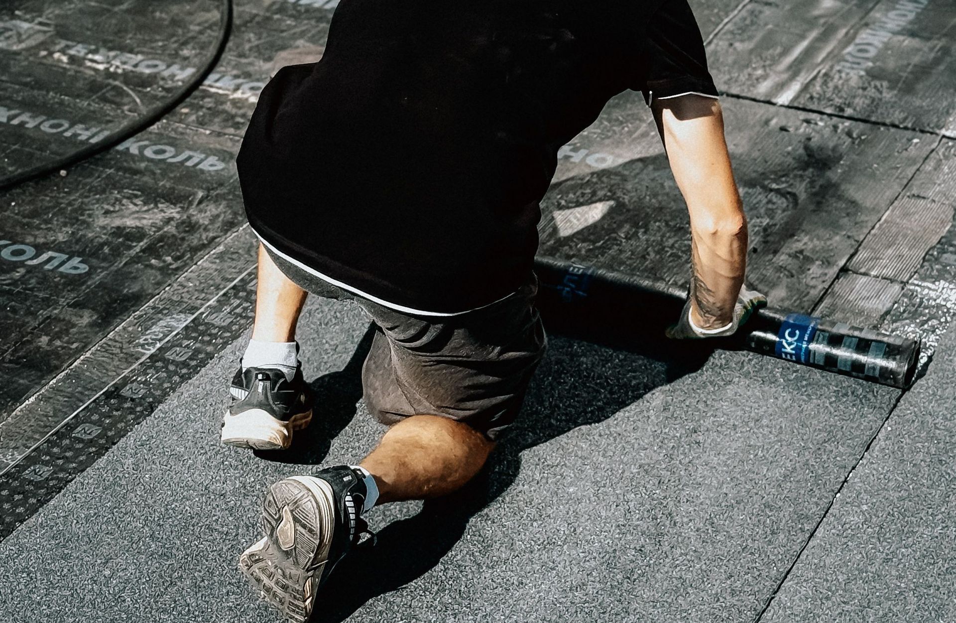 A construction worker installs asphalt roofing material under the sun, demonstrating professional craftsmanship.